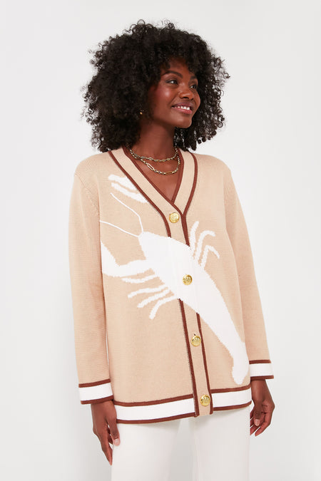 A woman styles a Tuckernuck oversized lobster cardigan with brown trim and a bold white lobster motif, pairing it with layered necklaces for a chic, preppy look.