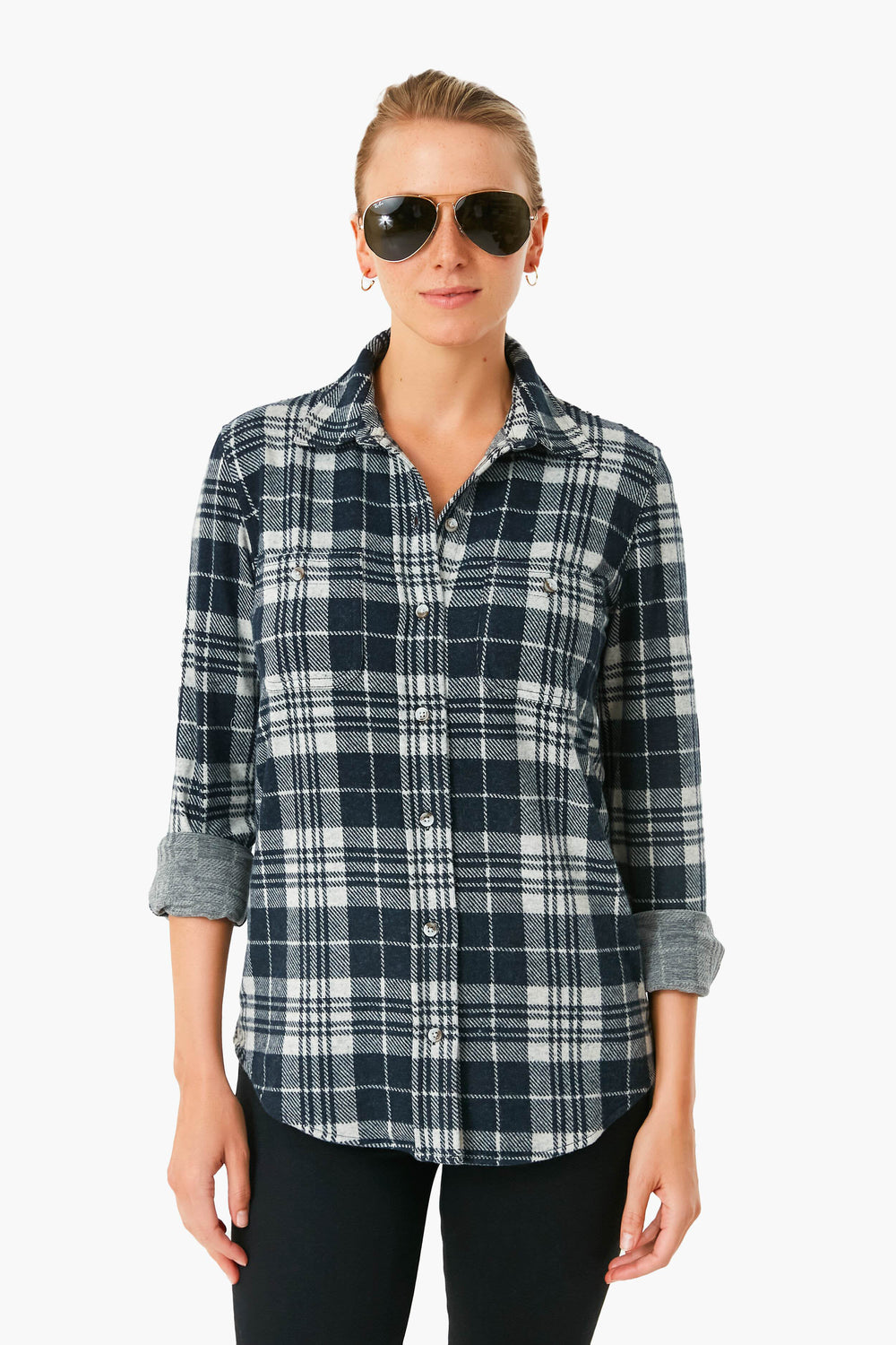 A woman faces forward wearing black sunglasses, black pants, and a Faherty Navy Plaid Sweater Shirt with rolled-up sleeves, highlighting the brand's soft flannel sustainable apparel.