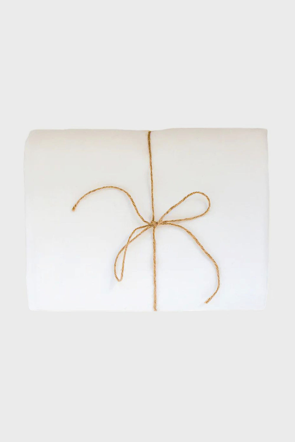 A folded white Madame de la Maison linen tablecloth, tied with a simple brown string bow and crafted from sustainable flax linen.
