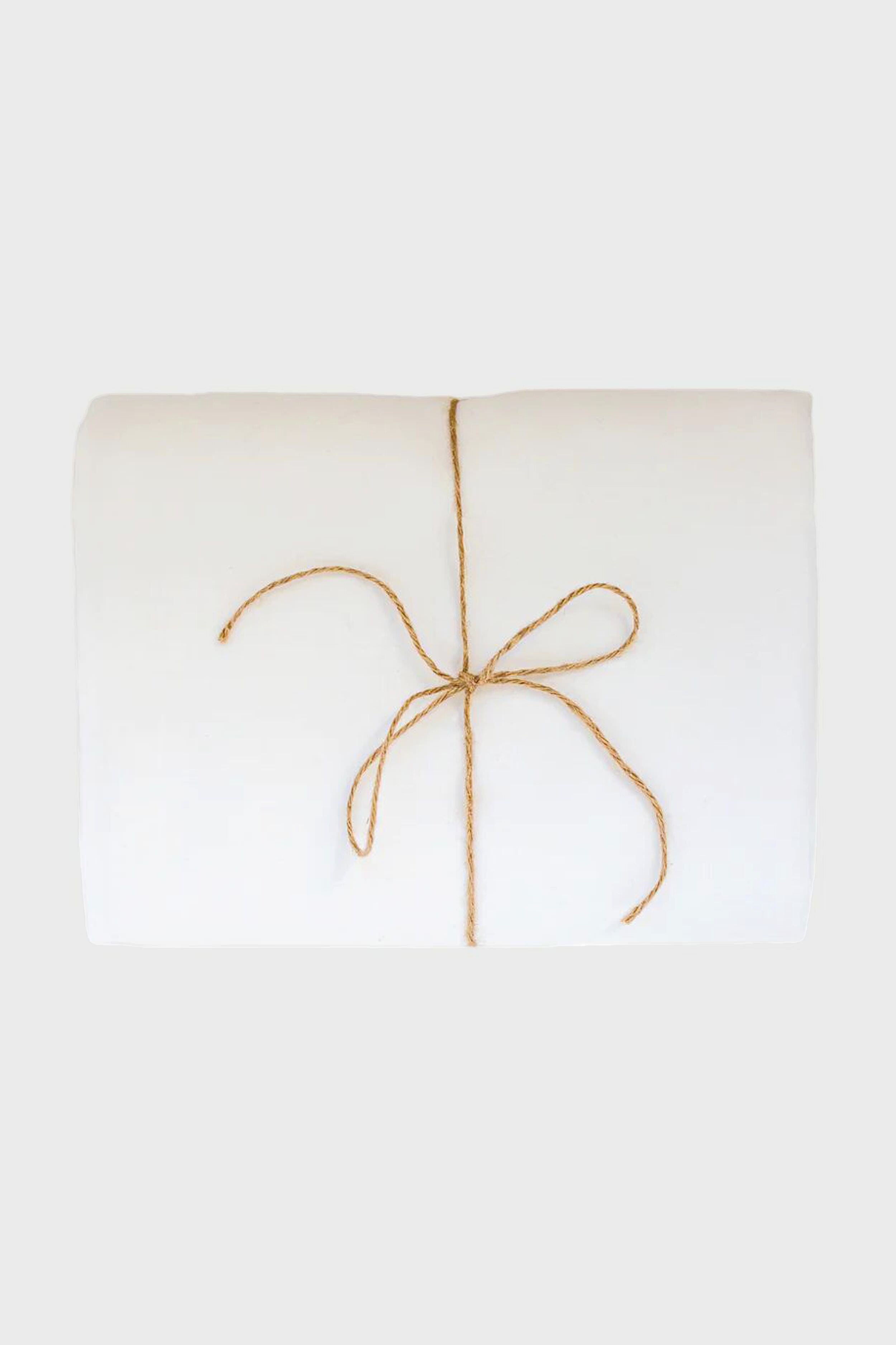 A folded white Madame de la Maison linen tablecloth, tied with a simple brown string bow and crafted from sustainable flax linen.