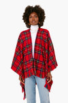 A woman creates a cozy and stylish look by wearing a David and Young red tartan poncho over a white turtleneck and light blue jeans.
