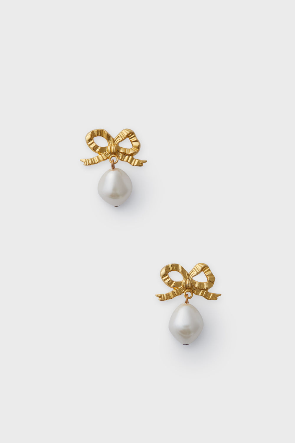 Gold bow-shaped earrings with dangling white pearls, these luxury baroque pearl earrings by Jennifer Behr are a stunning example of handmade jewelry.