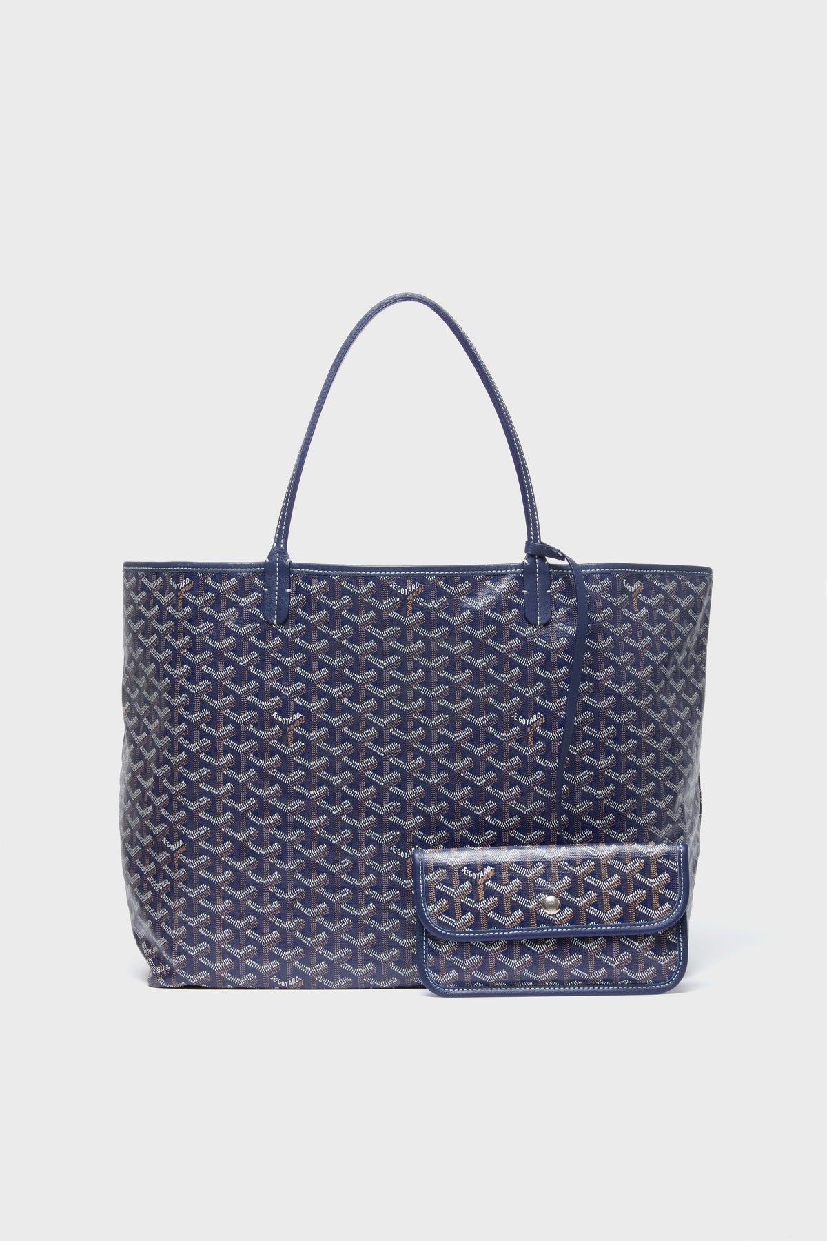 A large blue tote from the Tuckernuck Archive Collection features a geometric pattern on canvas, double handles, and a structured shape, paired with a matching small pouch.