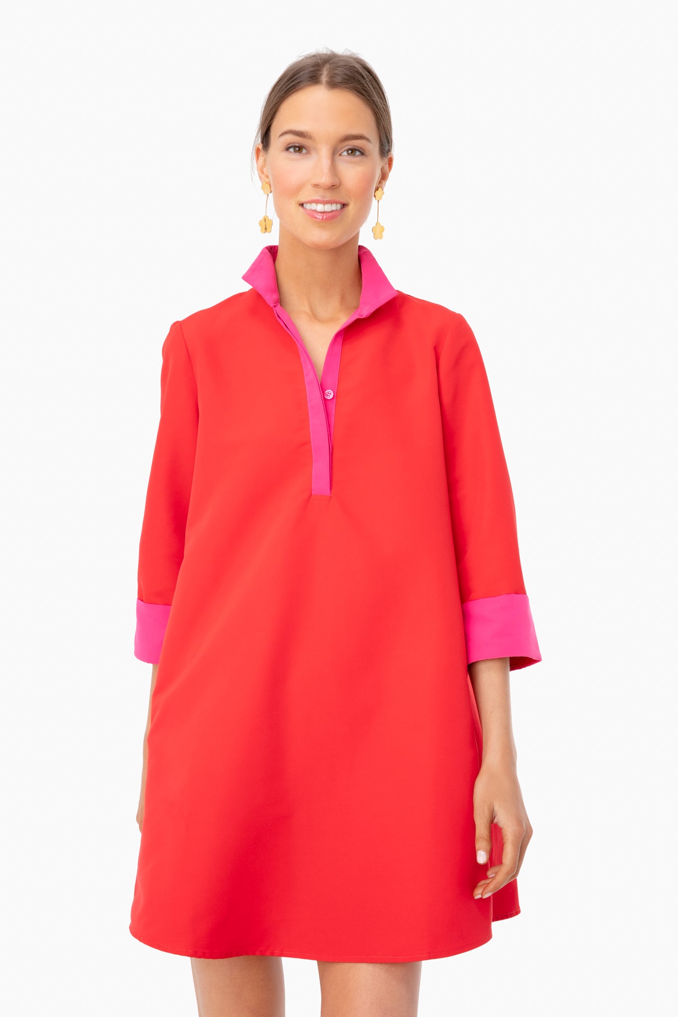 A woman wears a loose-fitting Tuckernuck Stone Megan Stand Collar Dress in red with pink collar and cuffs, gold earrings, and a neutral expression. The dress features a shift fit and structured fabric.