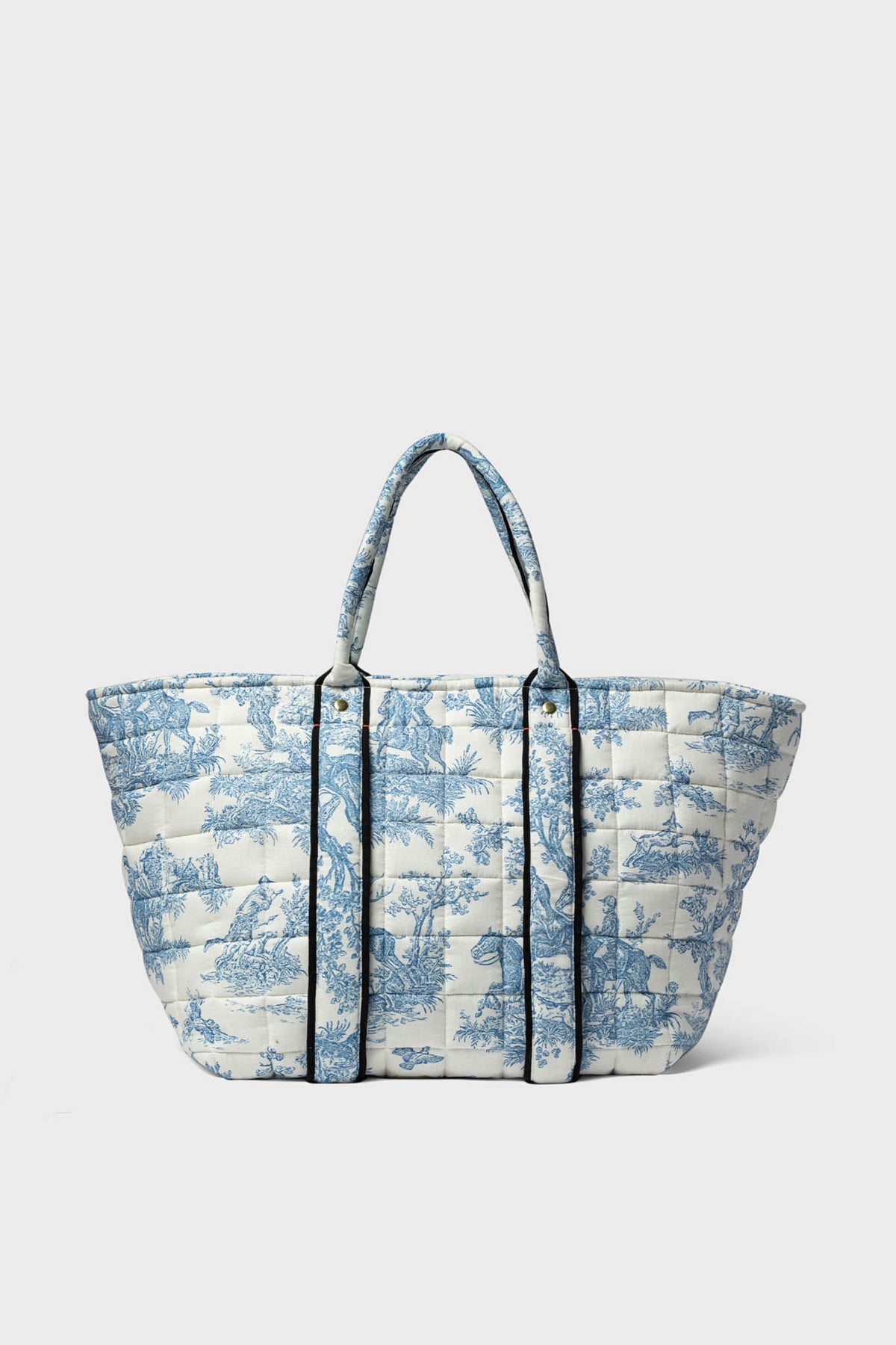 This Clare V oversized quilted linen tote features two handles, a blue and white pastoral toile print, and black vertical trim.
