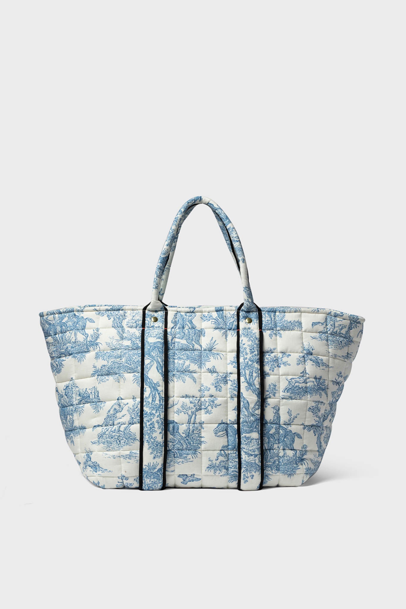 This Clare V oversized quilted linen tote features two handles, a blue and white pastoral toile print, and black vertical trim.