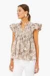 Woman in a Sea New York cheetah-print smocked top with flutter sleeves, ruffles, and tassel ties—styled with white pants and round statement earrings for a modern look.
