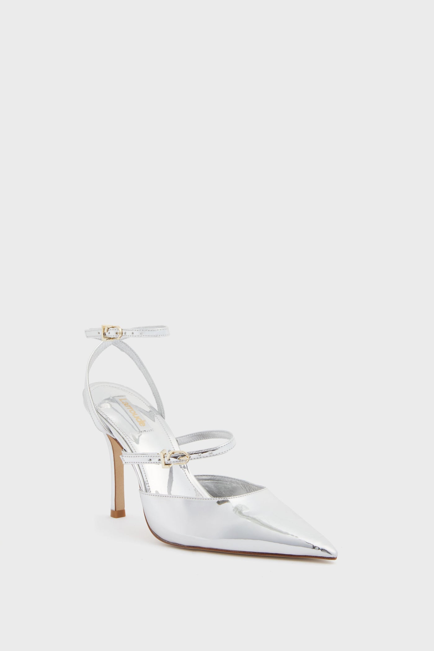 The Larroude silver stiletto heel features a pointed toe, two thin ankle straps with gold buckles, and a memory foam insole for comfort.