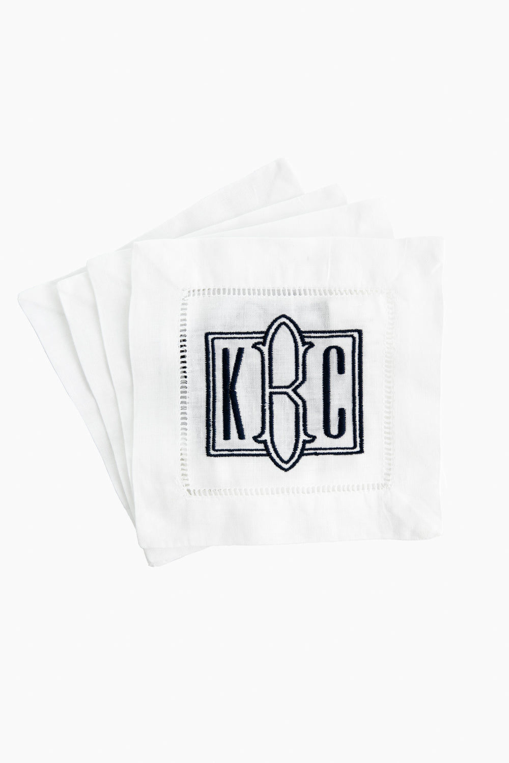 A stack of Caton's Wharf white Hemstitched Cocktail Napkins, each with an embroidered "K C" monogram and black eyeglass outline—an ideal personalized gift.