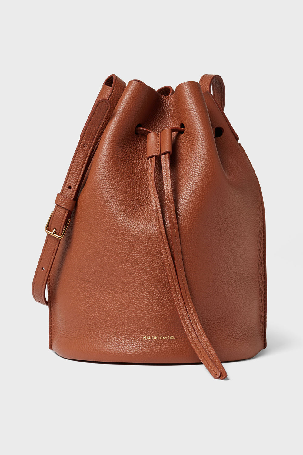 Mansur Gavriel's brown Italian leather bucket bag includes a drawstring closure, adjustable shoulder strap, and gold buckle.