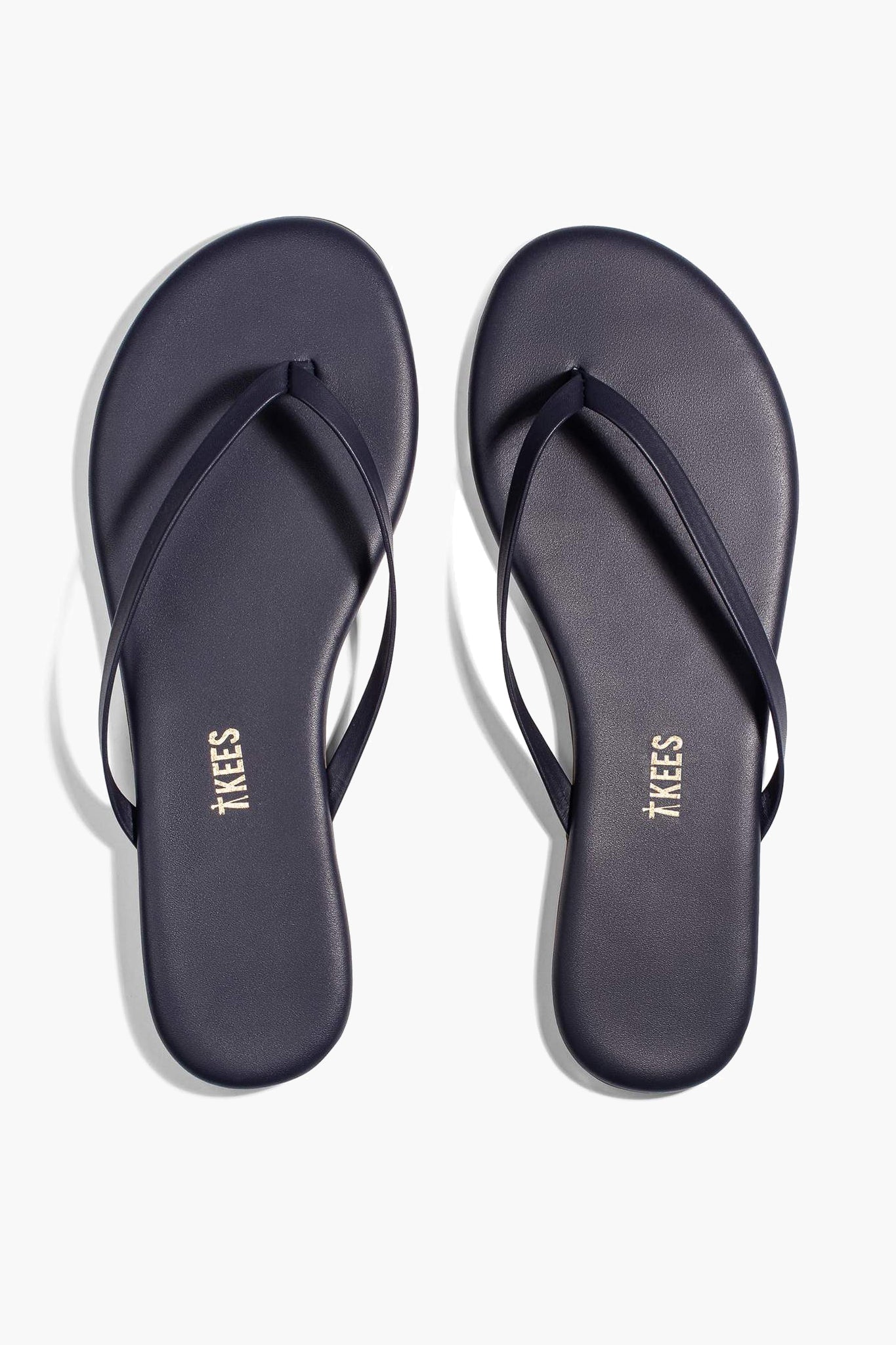 A pair of TKEES flip-flops in dark navy blue leather with thin straps, made in Brazil.