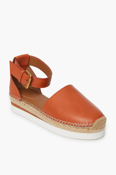 A See by Chloe orange leather espadrille platform sandal with an ankle strap, buckle closure, jute-wrapped sole, and white rubber outsole.