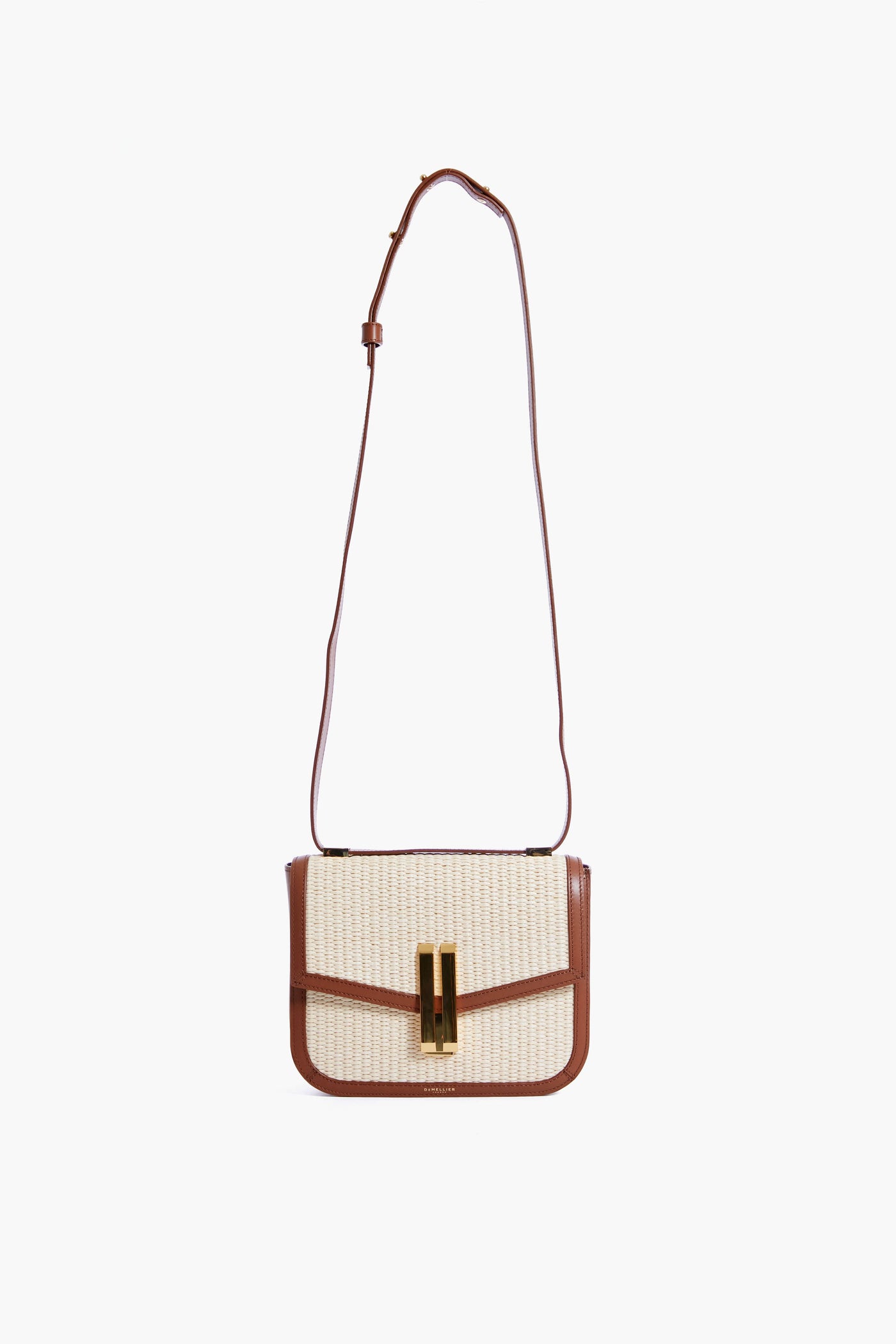 The Demellier Vancouver Crossbody Bag features a rectangular shape with a woven beige front, brown leather trim and strap, and a gold rectangular clasp. This handcrafted bag offers timeless style and elegance for any occasion.