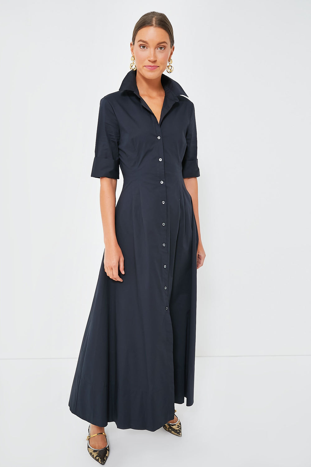 A woman wears the STAUD Joan Dress, a black cotton poplin shirt dress with a collar, button-down front, and short sleeves, paired with pointed flats.