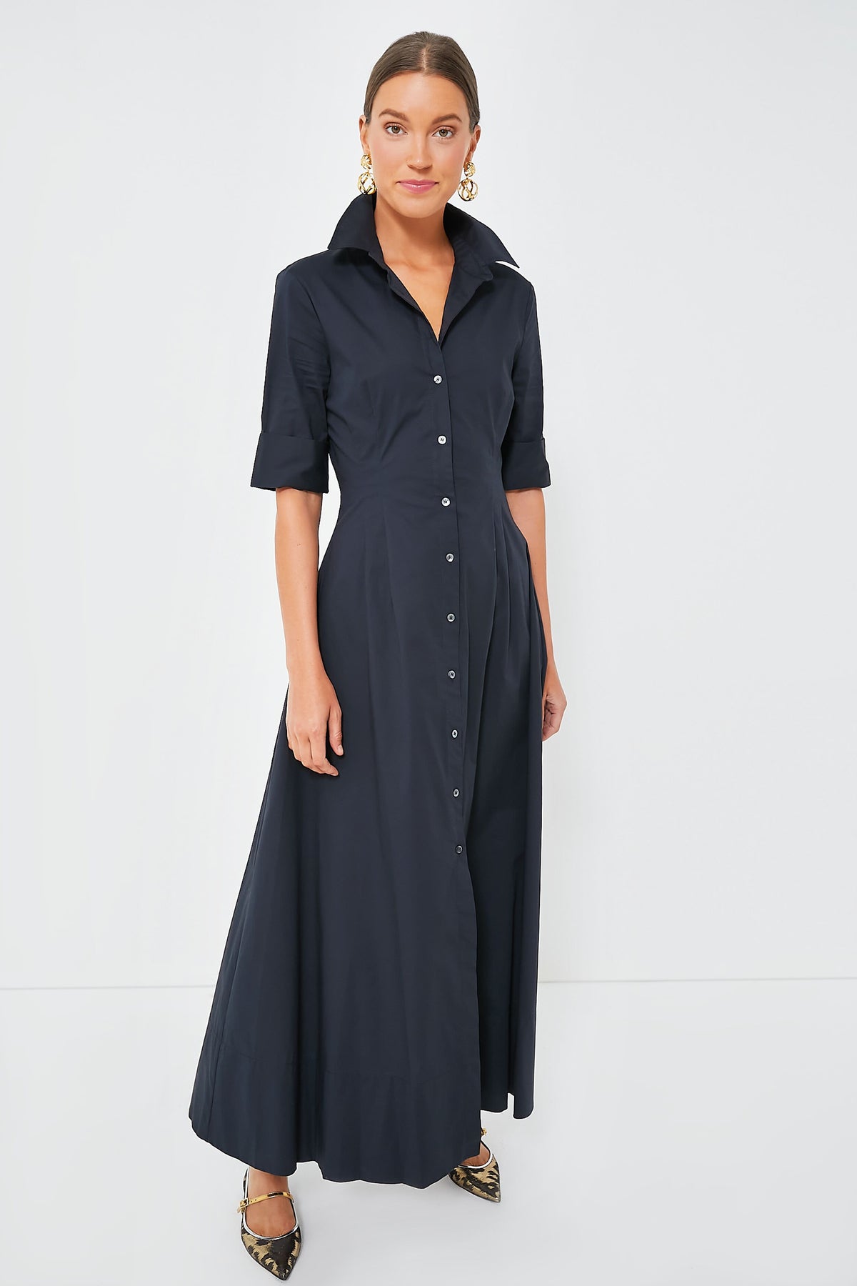 A woman wears the STAUD Joan Dress, a black cotton poplin shirt dress with a collar, button-down front, and short sleeves, paired with pointed flats.
