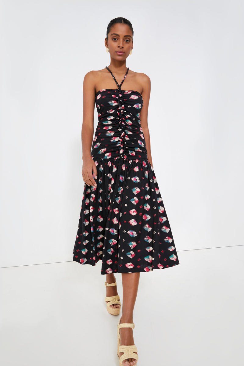 A woman stands confidently in a strapless, ruched Ulla Johnson black maxi dress with a colorful geometric print and beige platform sandals.