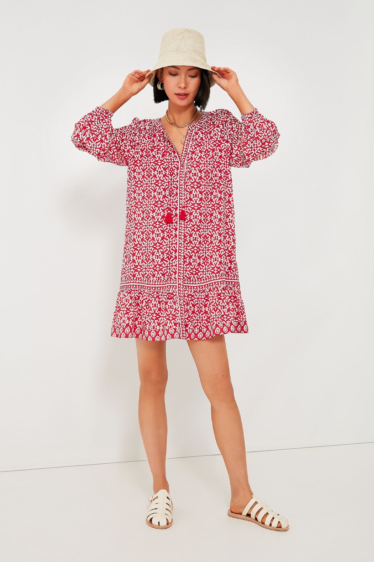A woman exudes effortless style in a boho-chic Vineyard Vines red travel mini dress, paired with white sandals and a light-colored hat.