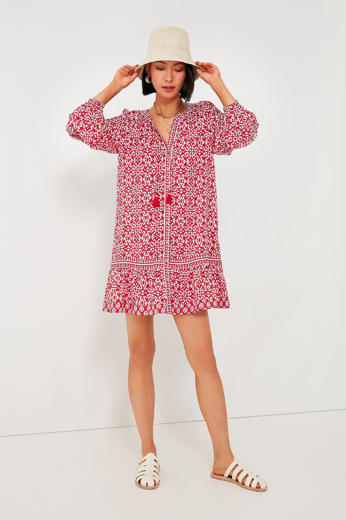 A woman exudes effortless style in a boho-chic Vineyard Vines red travel mini dress, paired with white sandals and a light-colored hat.