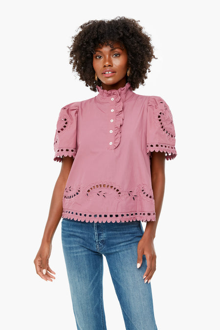 A woman wears the Sea New York Orchid Santos Top—a pink, short-sleeve, high-neck blouse with eyelet detail from the India Collection—paired with blue jeans.