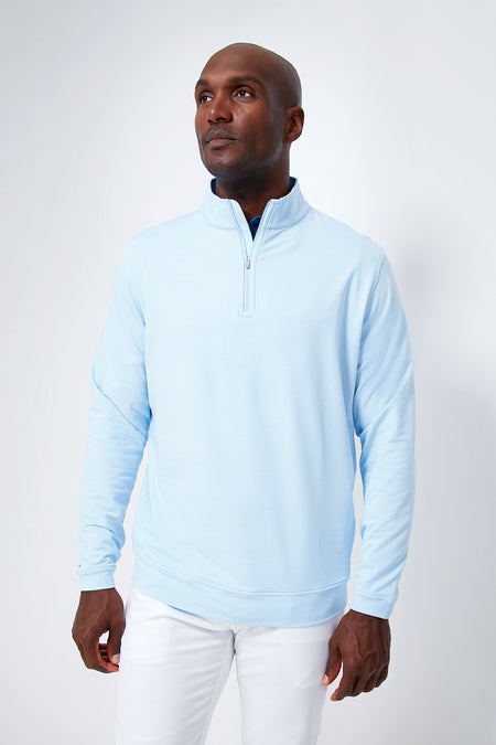 A man stands confidently in a light blue Peter Millar quarter-zip pullover and white pants, highlighting classic style and comfort with the look of stretch French terry.