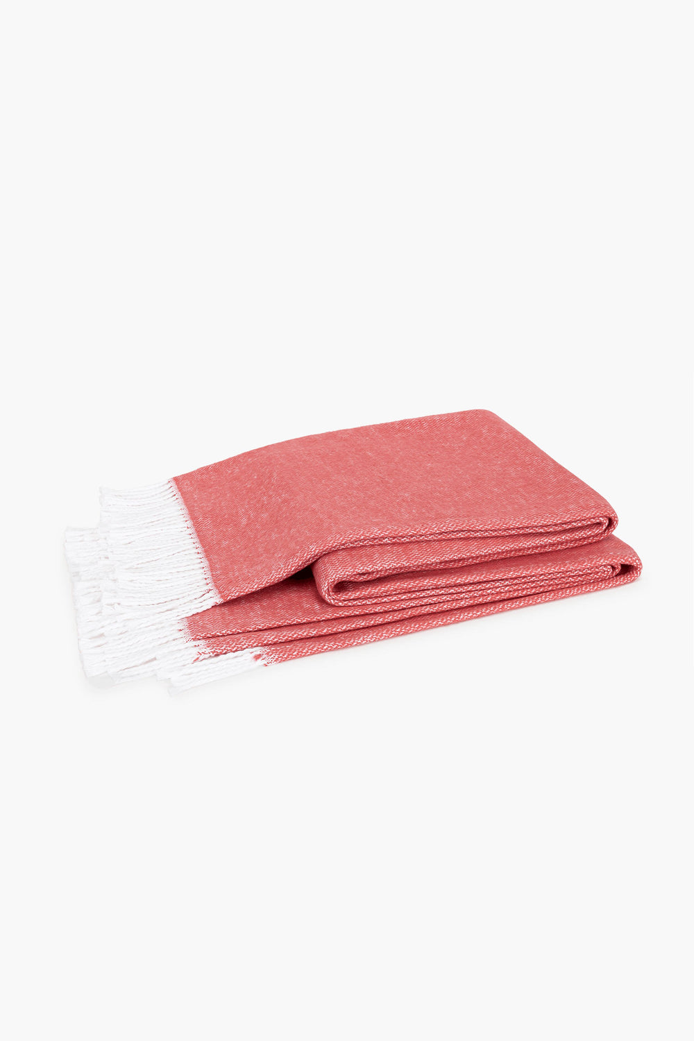 A soft cotton throw by Matouk in deep coral, featuring white fringed edges, brings a cozy touch to any space.