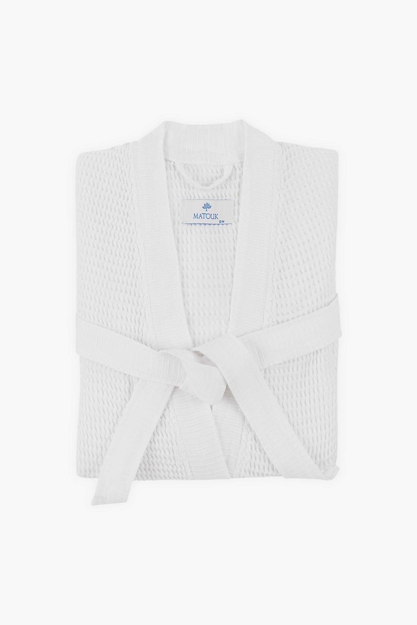 A neatly folded white Matouk Turkish waffle bathrobe with a front-tied belt and a label displaying the brand name.
