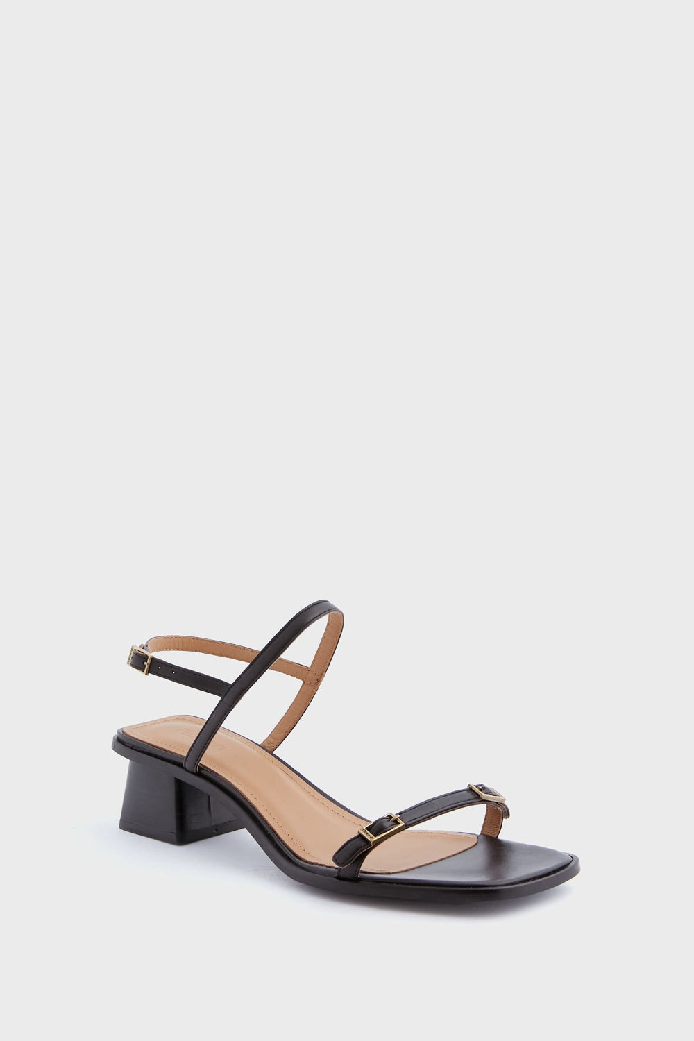 The Flattered Black Jonah Heels are handmade leather sandals featuring a low block heel, ankle strap, and sleek black strappy design.