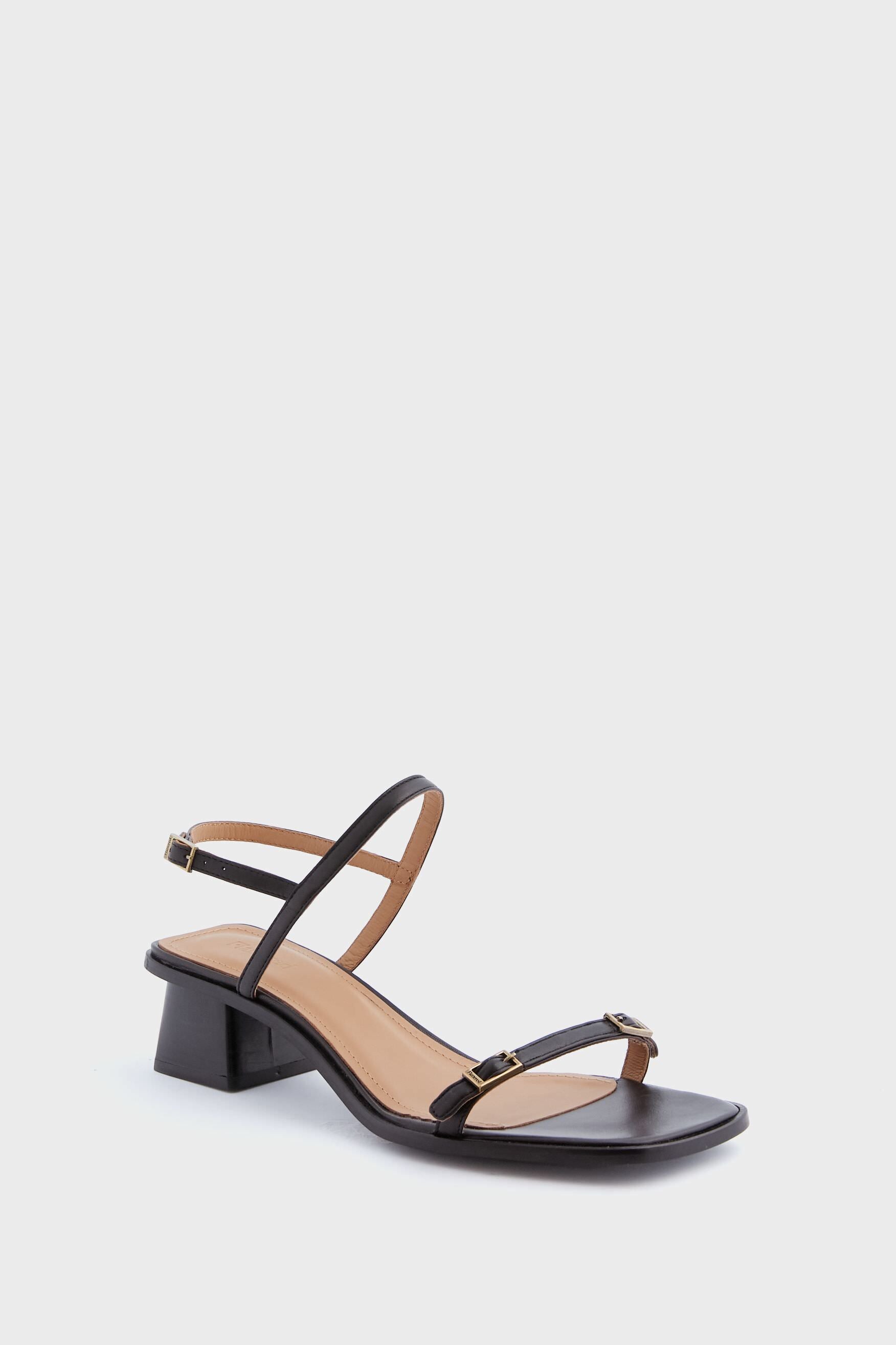 The Flattered Black Jonah Heels are handmade leather sandals featuring a low block heel, ankle strap, and sleek black strappy design.