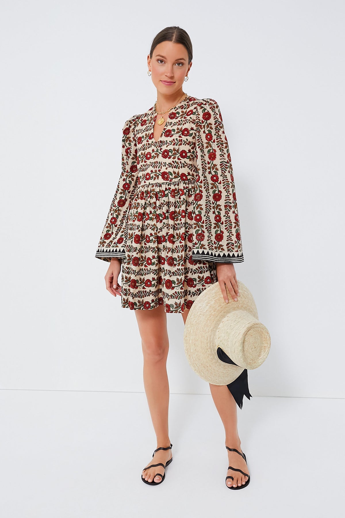 A woman in an Alix of Bohemia cotton dress holds a large straw hat with a black ribbon, embodying stylish simplicity.