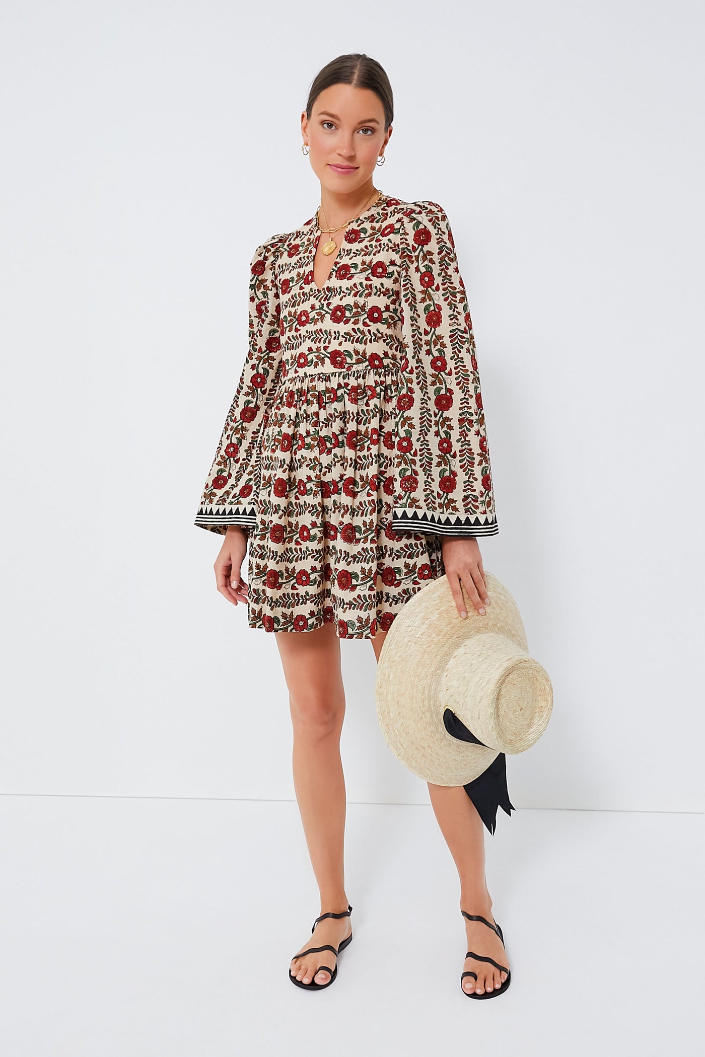 A woman in an Alix of Bohemia cotton dress holds a large straw hat with a black ribbon, embodying stylish simplicity.