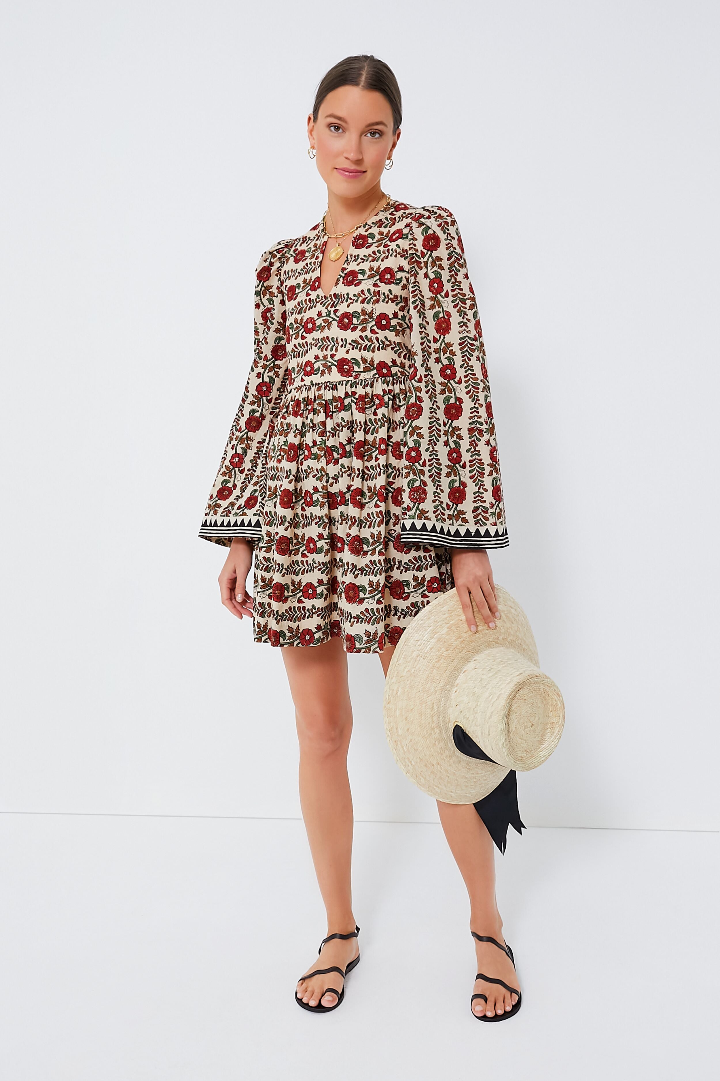 A woman in an Alix of Bohemia cotton dress holds a large straw hat with a black ribbon, embodying stylish simplicity.