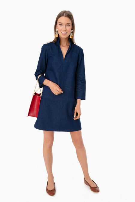 A woman wears a dark blue Tuckernuck Clifton Dress featuring a stand collar and elbow-length sleeves, styled with brown flats, statement earrings, and a red handbag.
