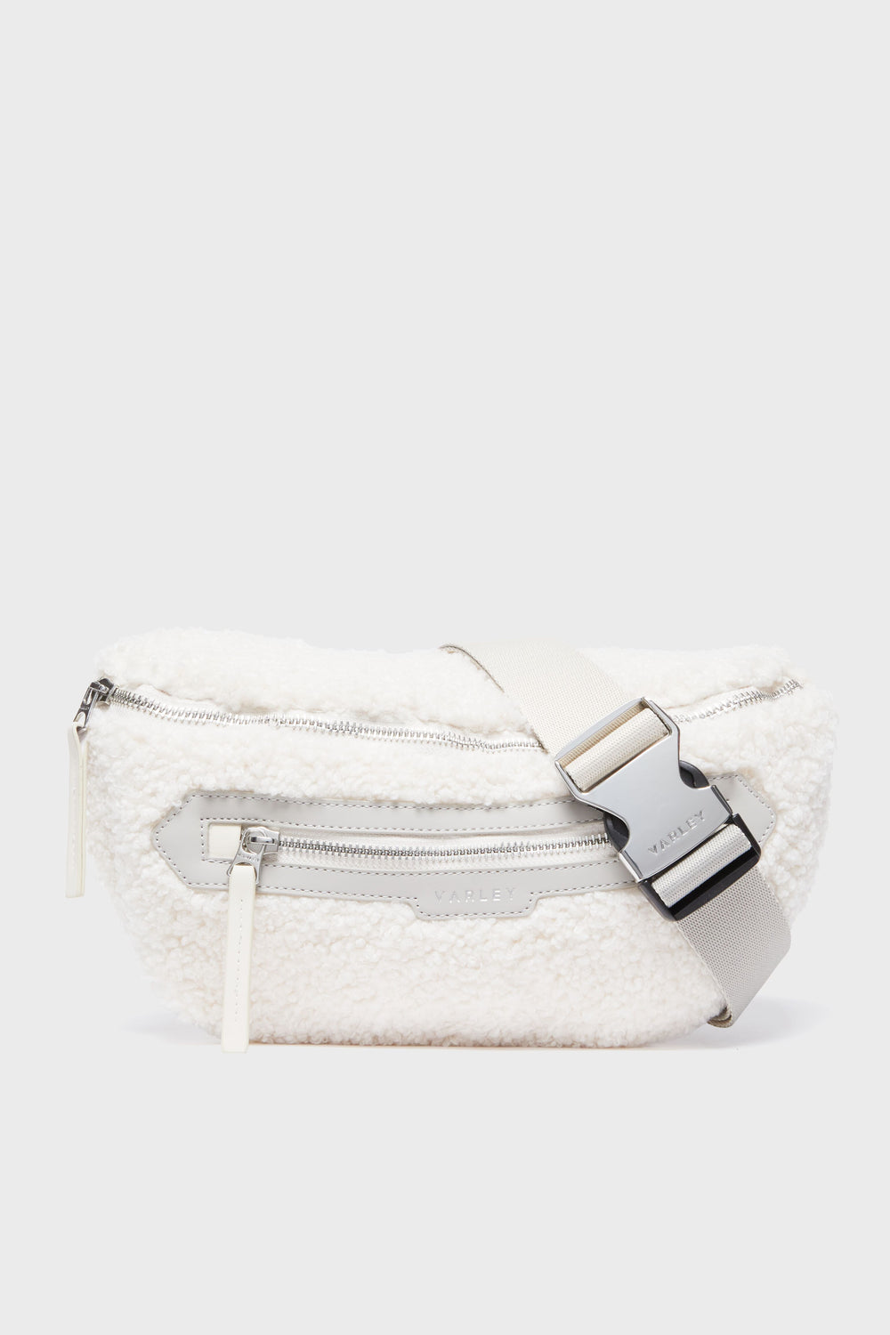 The Varley Sandshell Kansa Belt Bag is a white sherpa fanny pack with a silver zipper, spacious front zip pocket, and an adjustable strap with an engraved metal buckle—ideal for carrying essentials in style.