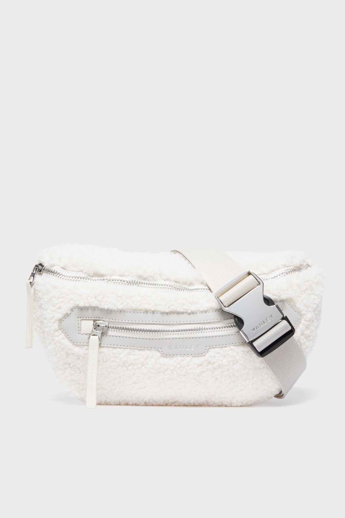 The Varley Sandshell Kansa Belt Bag is a white sherpa fanny pack with a silver zipper, spacious front zip pocket, and an adjustable strap with an engraved metal buckle—ideal for carrying essentials in style.