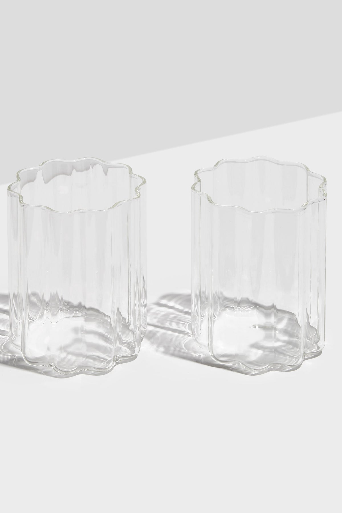 Two FAZEEK scalloped-edged rippled glasses sit side by side on a white surface, elegantly displaying their signature wave design.