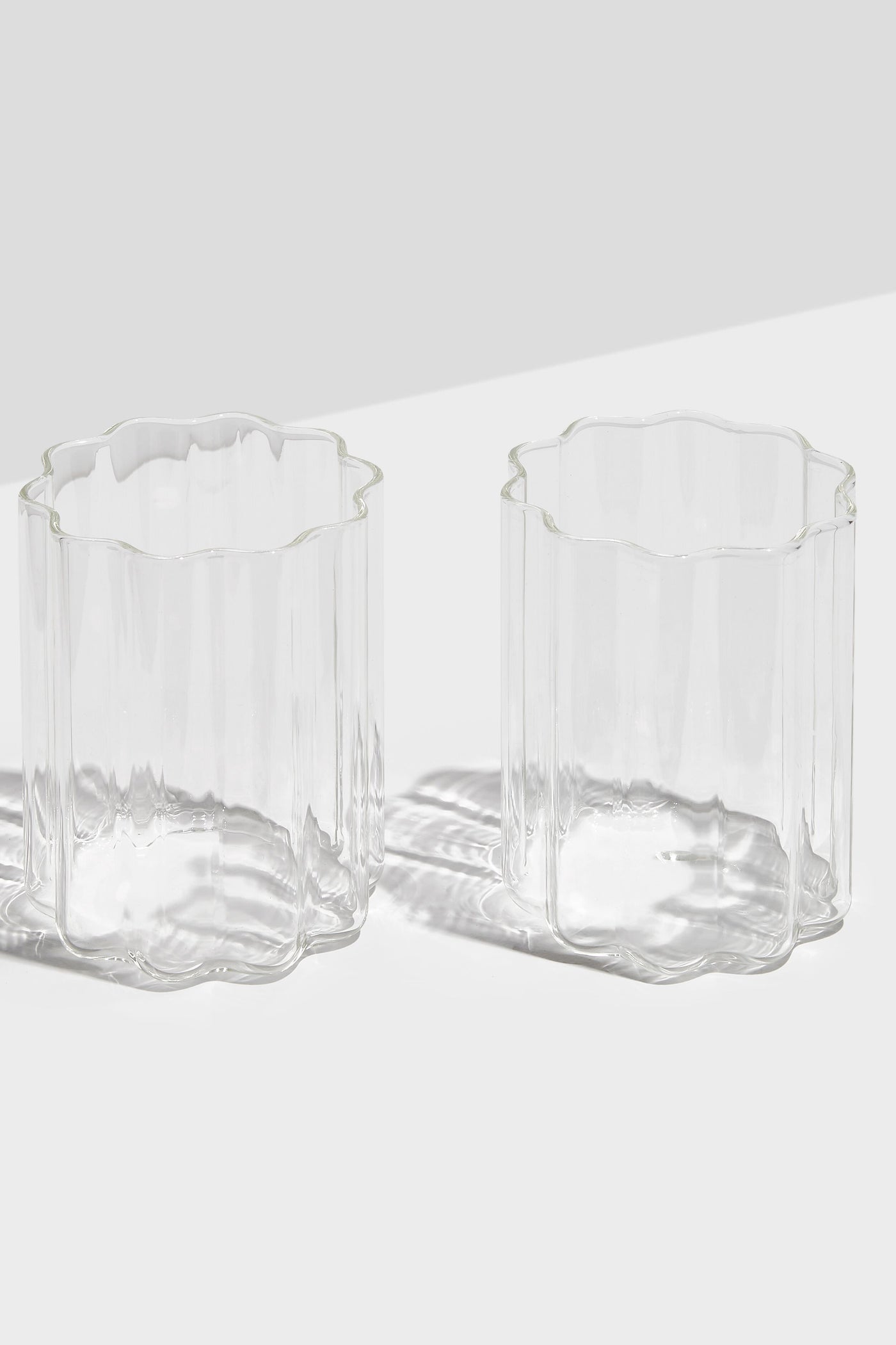 Two FAZEEK scalloped-edged rippled glasses sit side by side on a white surface, elegantly displaying their signature wave design.