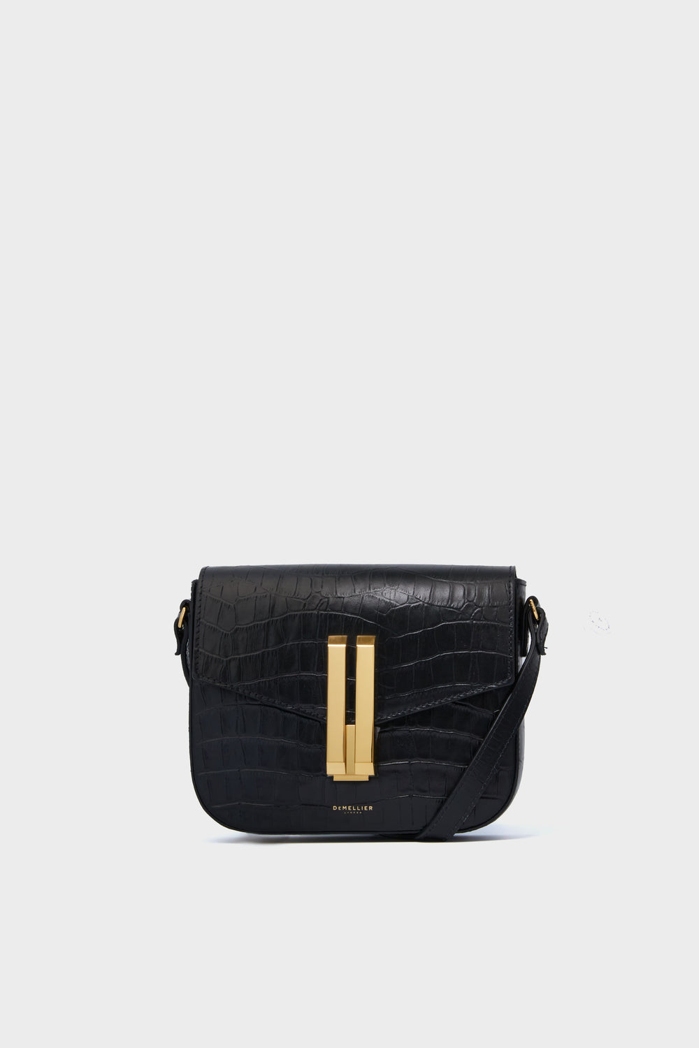 A Demellier Black Croc Small Vancouver Bag, a handcrafted leather handbag with a gold-tone rectangular clasp and adjustable crossbody strap, is displayed.