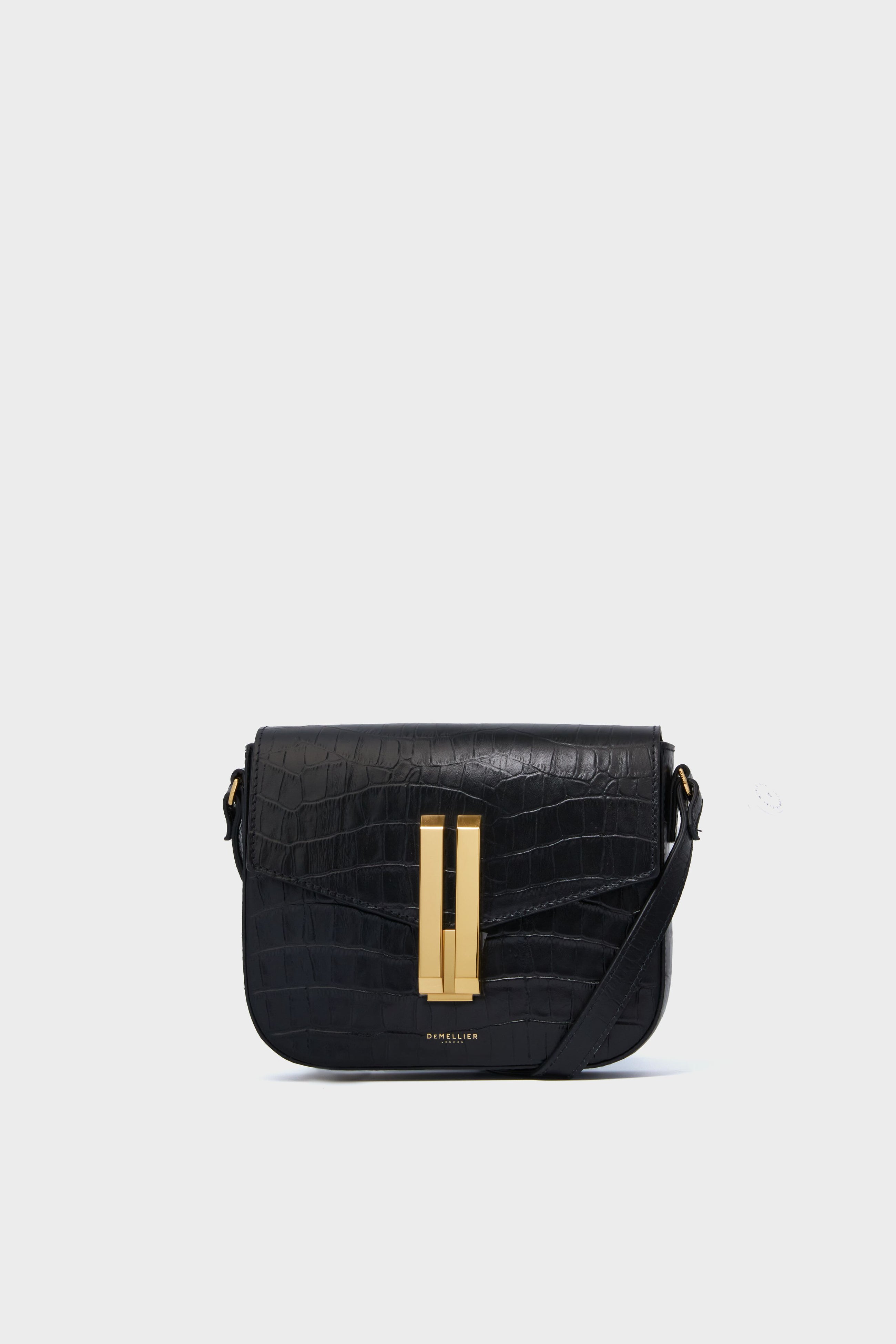 A Demellier Black Croc Small Vancouver Bag, a handcrafted leather handbag with a gold-tone rectangular clasp and adjustable crossbody strap, is displayed.