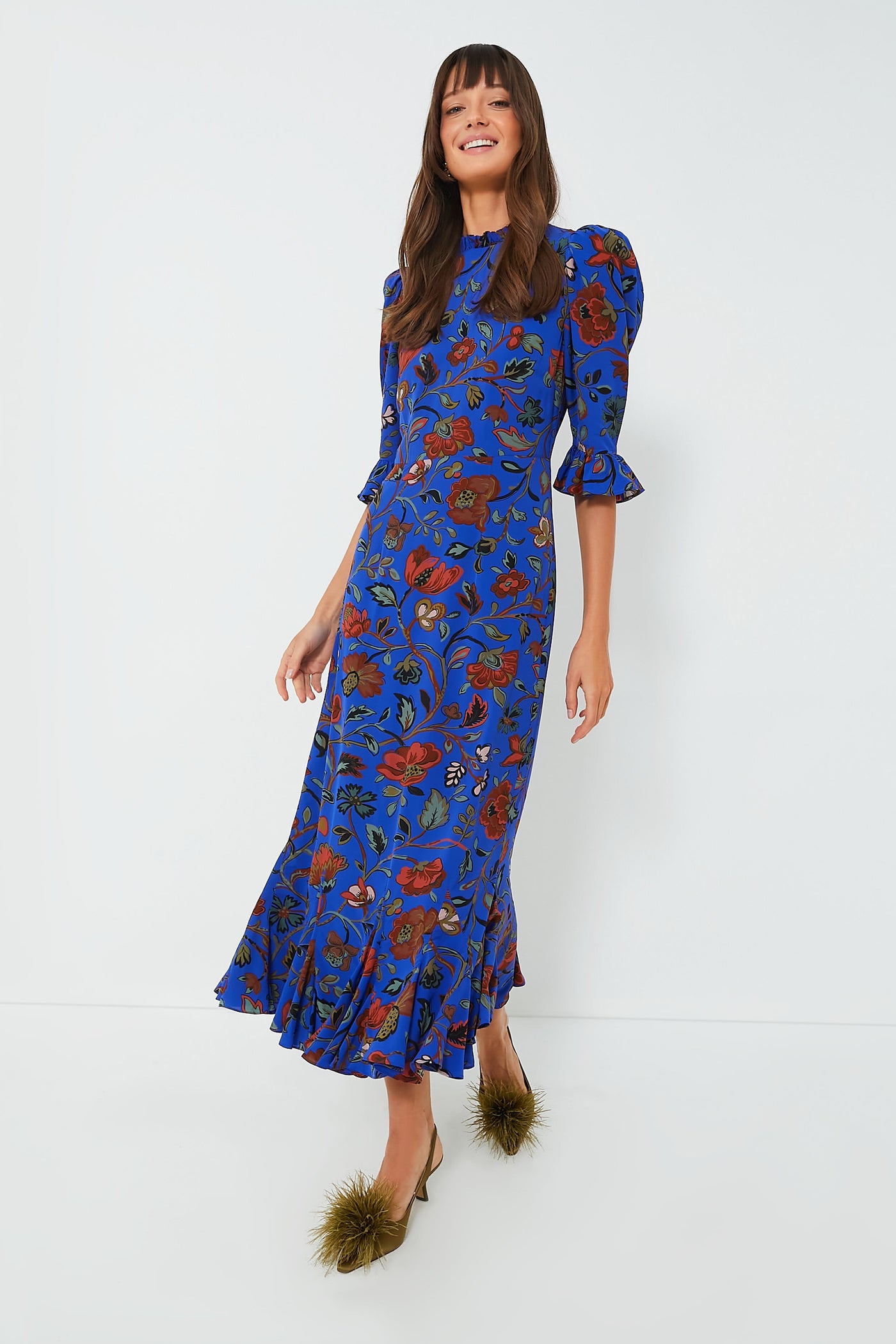 A woman wears the elegant RHODE Royal Vichy Vose Felix Dress in blue—a slim-fit midi with a ruffled neckline.