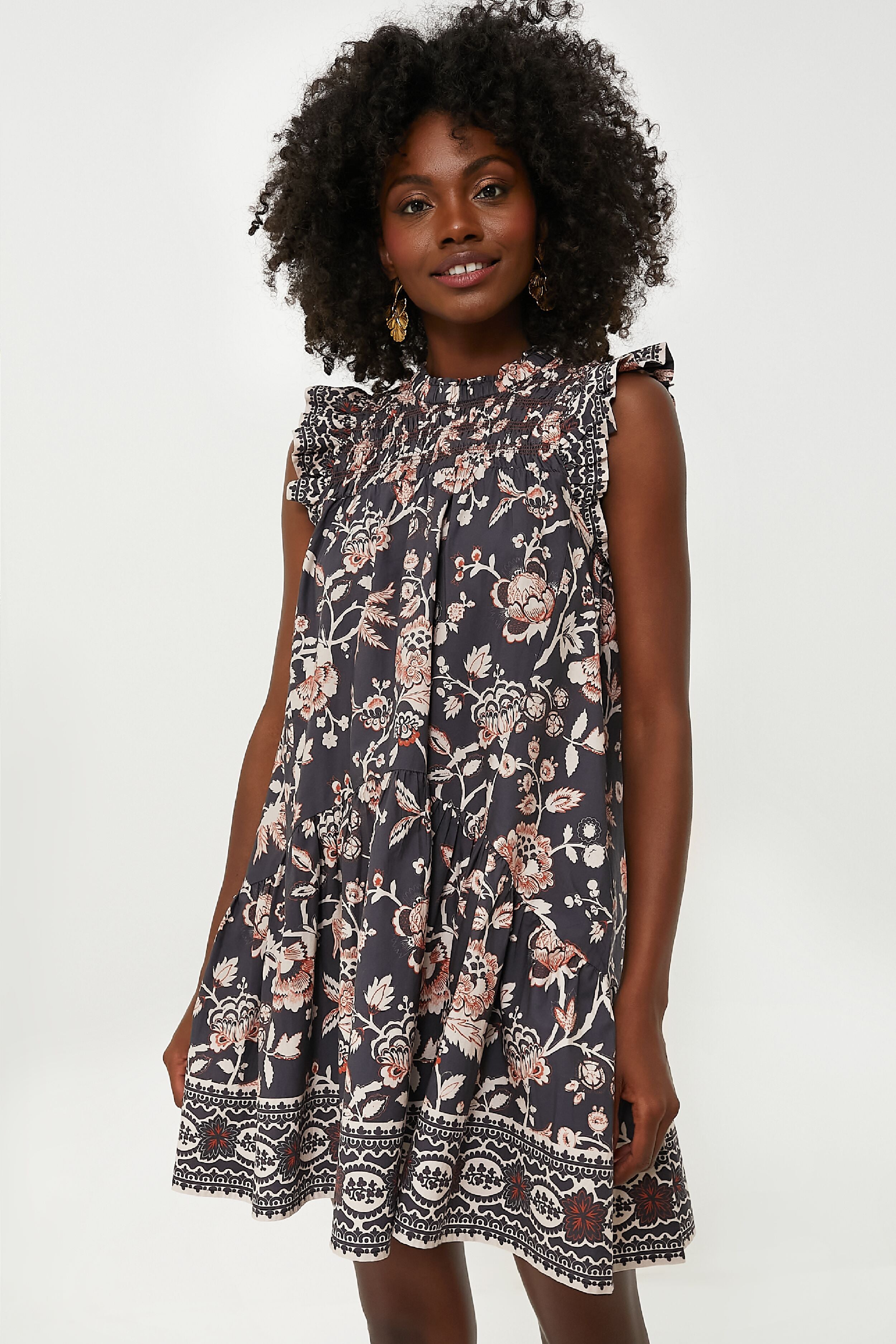 A woman wears the Love the Label Viola Dress—a navy blue, cotton floral mini dress with ruffled shoulders.