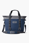 A navy blue and gray YETI soft cooler bag featuring a shoulder strap, two handles, and visible YETI logos. This leak-resistant cooler from YETI combines durability with convenience.