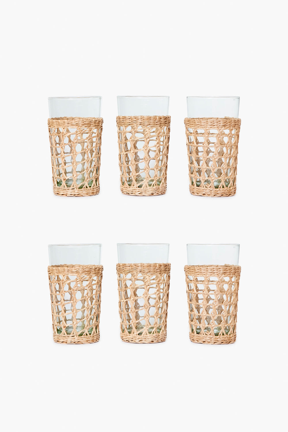 The Seagrass set includes six clear glass tumblers in woven rattan sleeves, arranged in two rows of three—a stylish glassware set that brings coastal charm to any space.