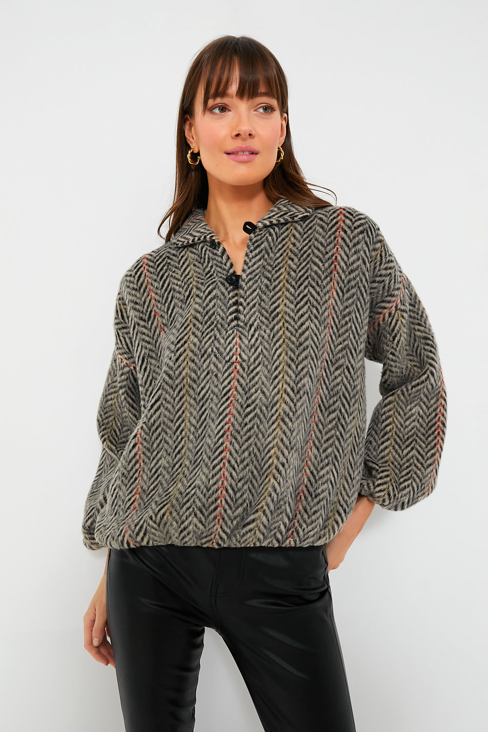 A woman stands confidently in THE GREAT. vintage-inspired pullover with chevron stripes and black pants.