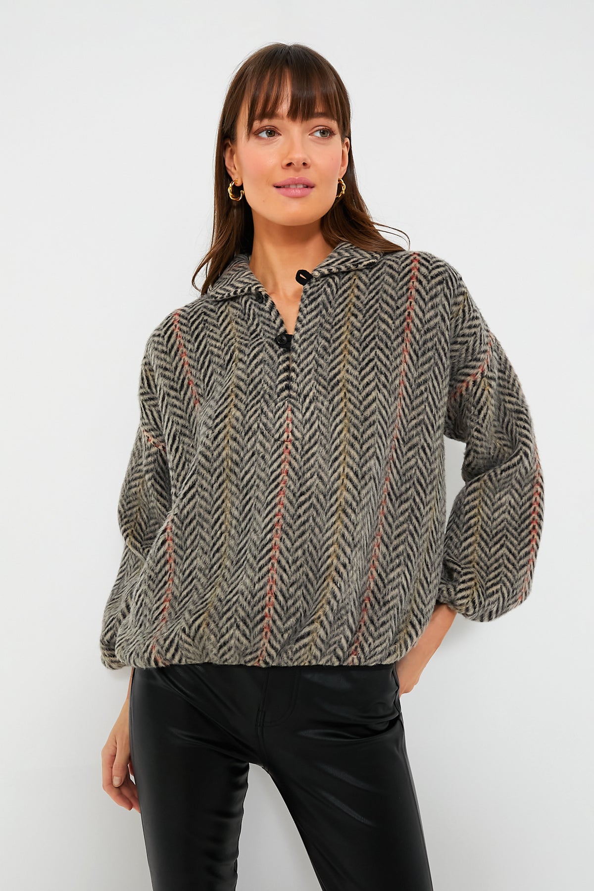 A woman stands confidently in THE GREAT. vintage-inspired pullover with chevron stripes and black pants.