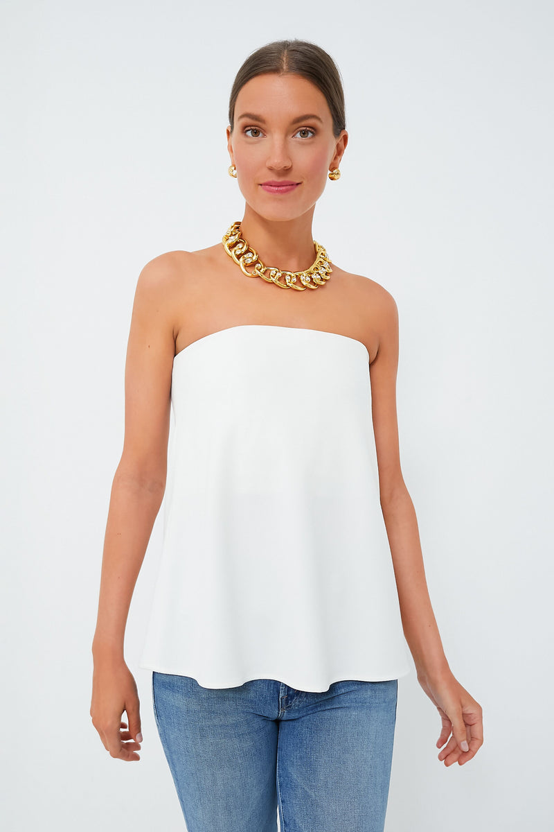 A woman in a Tuckernuck white flowy strapless top with built-in bra, blue jeans, gold chain necklace, and gold earrings.