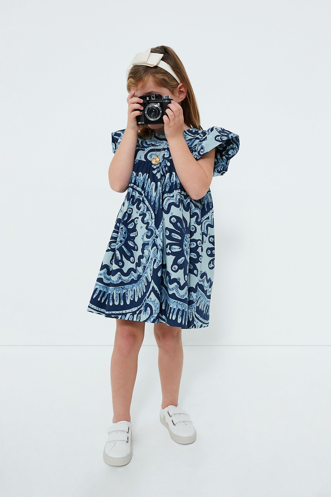 A girl in a Sea New York Blue Charlough Print Flutter Sleeve Dress holds a camera.