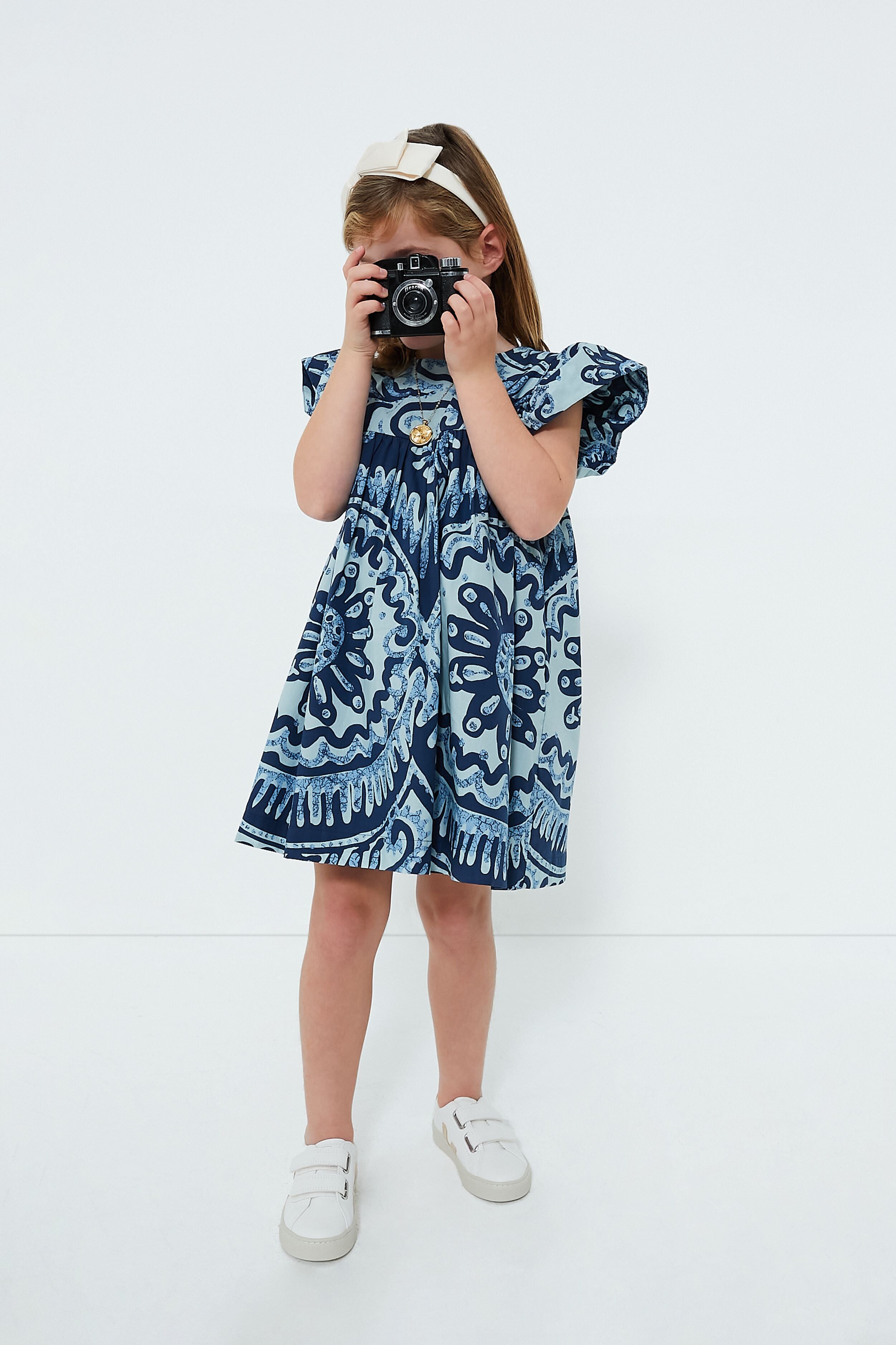 A girl in a Sea New York Blue Charlough Print Flutter Sleeve Dress holds a camera.