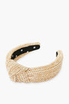 A Lele Sadoughi woven raffia headband featuring a front knot and black inner lining with small white flower patterns.