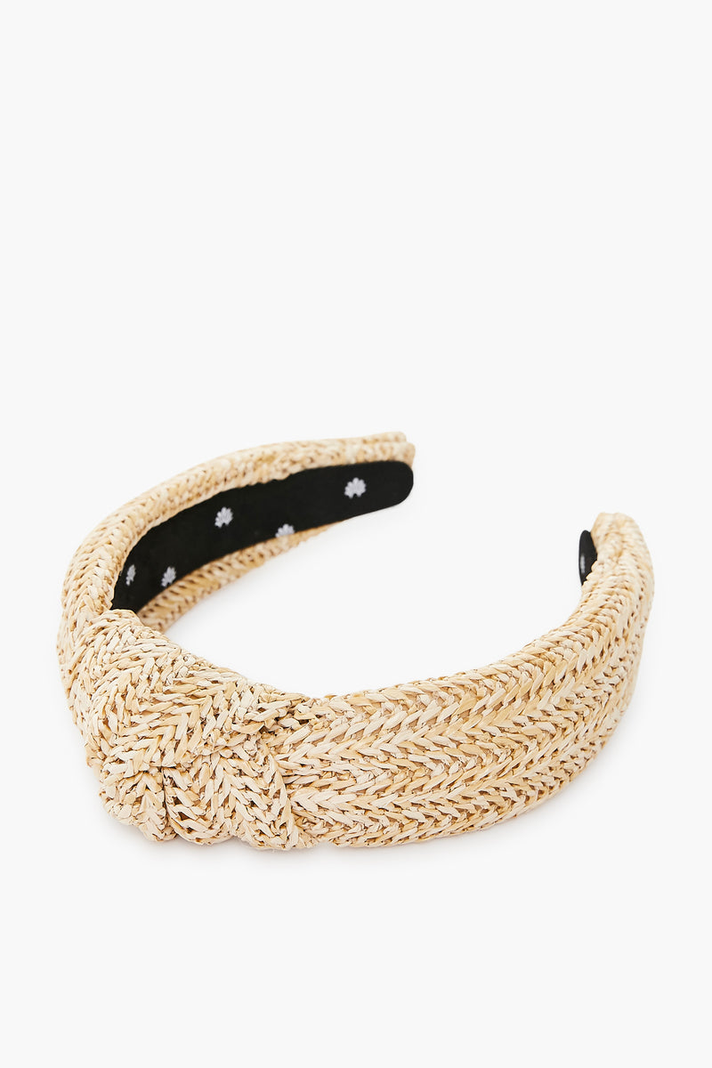 A Lele Sadoughi woven raffia headband featuring a front knot and black inner lining with small white flower patterns.