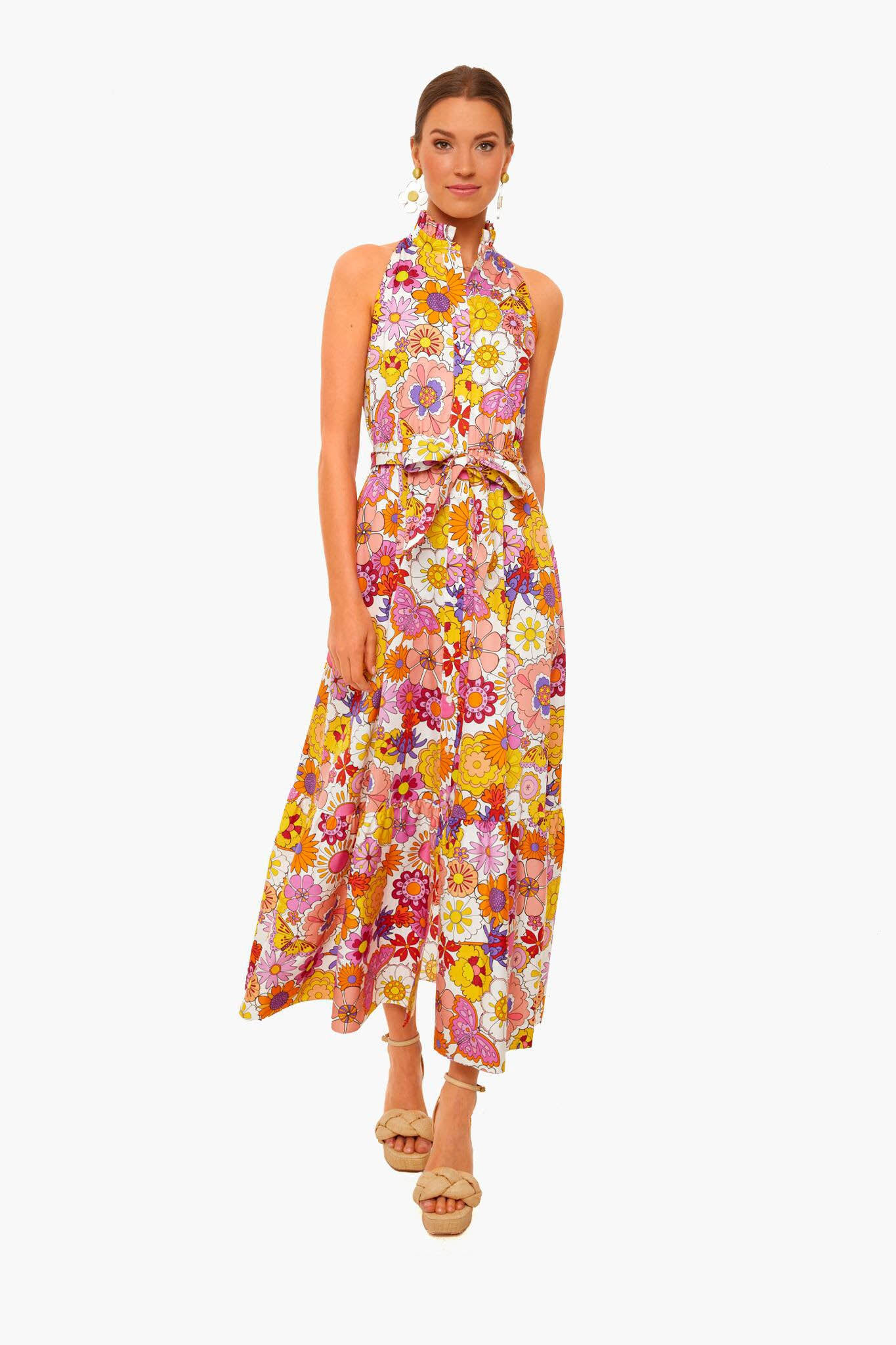 A woman wears a Borgo de Nor sleeveless, ankle-length dress with a colorful floral pattern, belted at the waist, paired with beige sandals.
